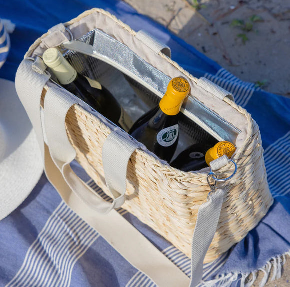 Straw beach bag with wine bottles on a blue blanket.