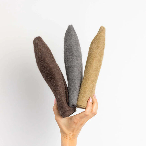 Two hands holding three rolls of felt in brown, gray, and beige colors, against a plain white background.