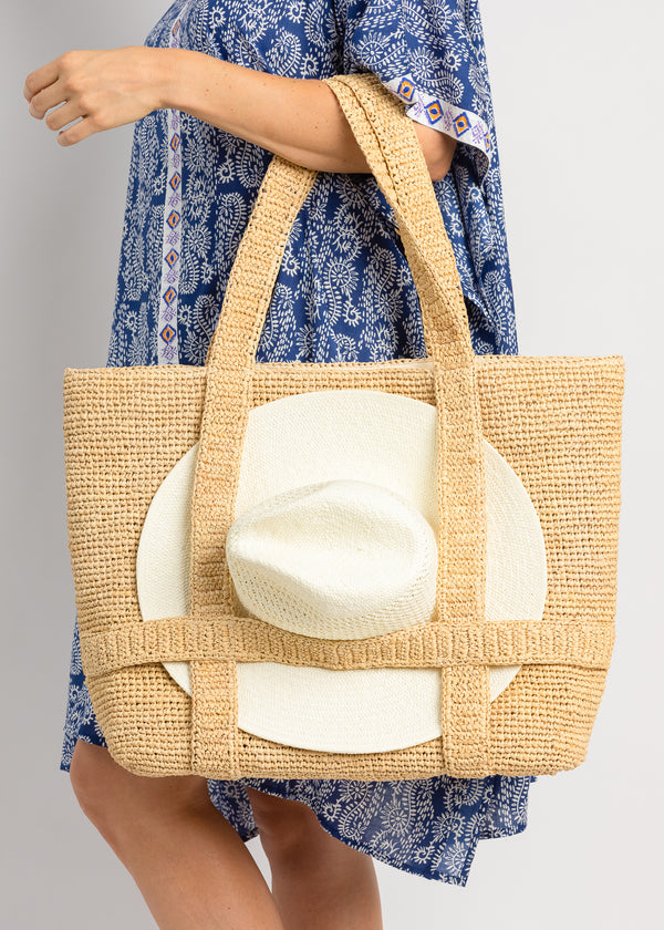 Model holding a straw tote bag with a white sun hat attached