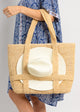 Model holding a straw tote bag with a white sun hat attached