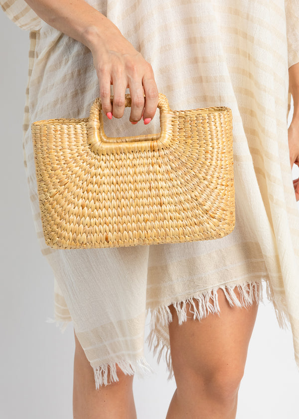 Model holding rectangular hyacinth bag and wearing a striped kaftan