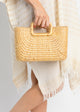 Model wearing tan and white kaftan holding a rectangular straw bag