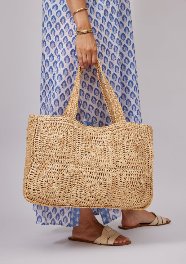 Model holding a straw tote and wearing a blue kaftan