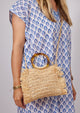 Model wearing straw crossbody bag with fringe detail and round tortoise handles