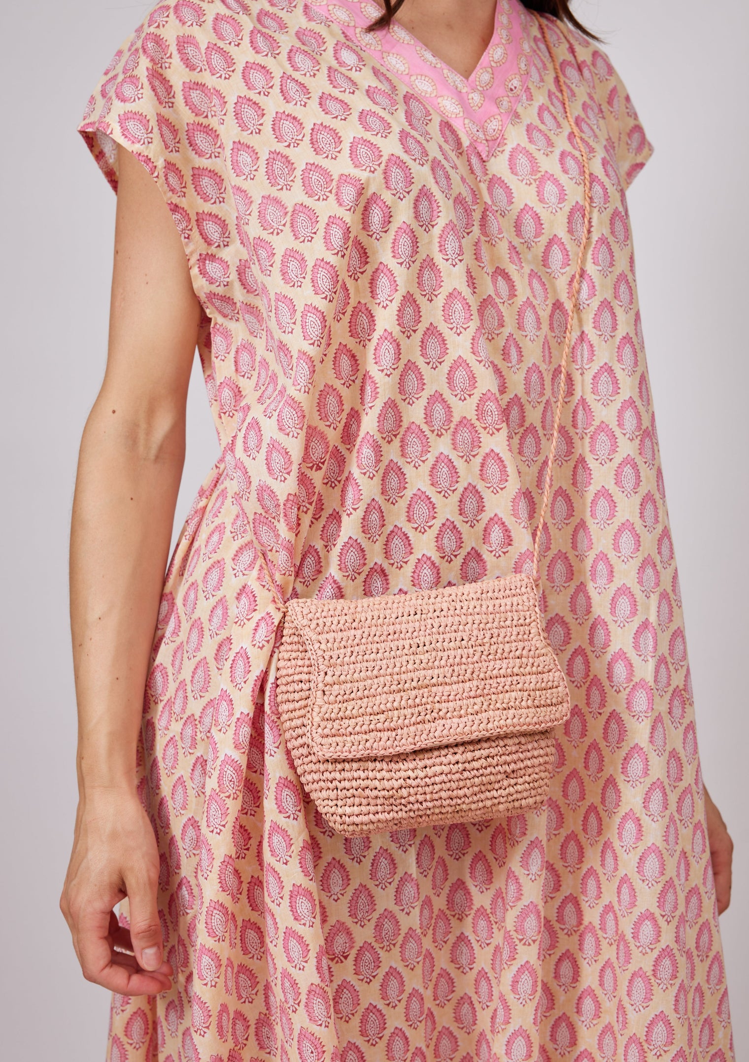 Small pink straw crossbody bag on model wearing pink kaftan
