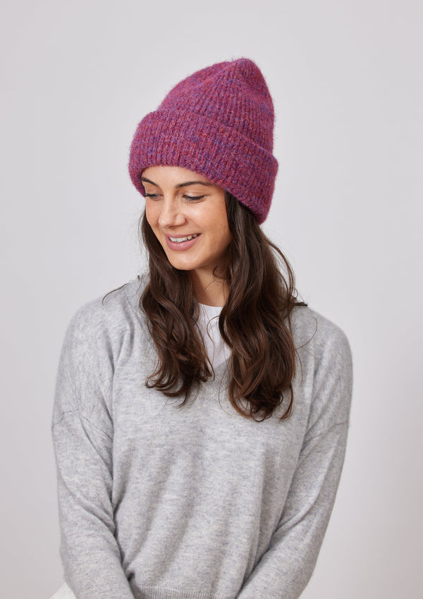 Model wearing raspberry colored cuff beanie and looking down to right 