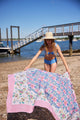 Model putting pink and blue beach blanket on sand