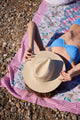Model laying on beach blanket with a hat over her face