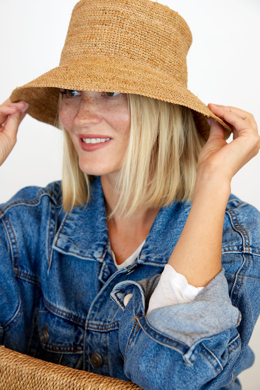 Model smiling and holding brim of straw bucket hat