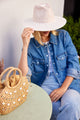 model holding the brim of her hat and sitting at a table with a small straw bag