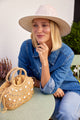 model sitting at a table, wearing a straw hat and small straw bag