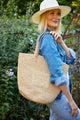 Model holding straw bag with leather handles and a denim outfit