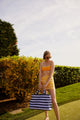 Model wearing yellow floral sarong and holding blue and lavender striped bag