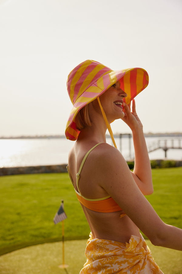 Model wearing yellow and coral striped hat with chinstrap