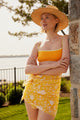 Model wearing a yellow floral sarong while leaning on a tree