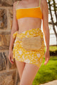 Close up of model wearing a yellow floral sarong and straw belt bag