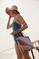 Model wearing blue bathing suit and holding colorful tote