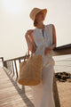 Model holding a straw tote and wearing a white outfit