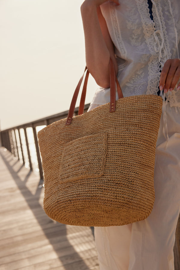 Close up of model wearing straw tote with a pocket on the outside