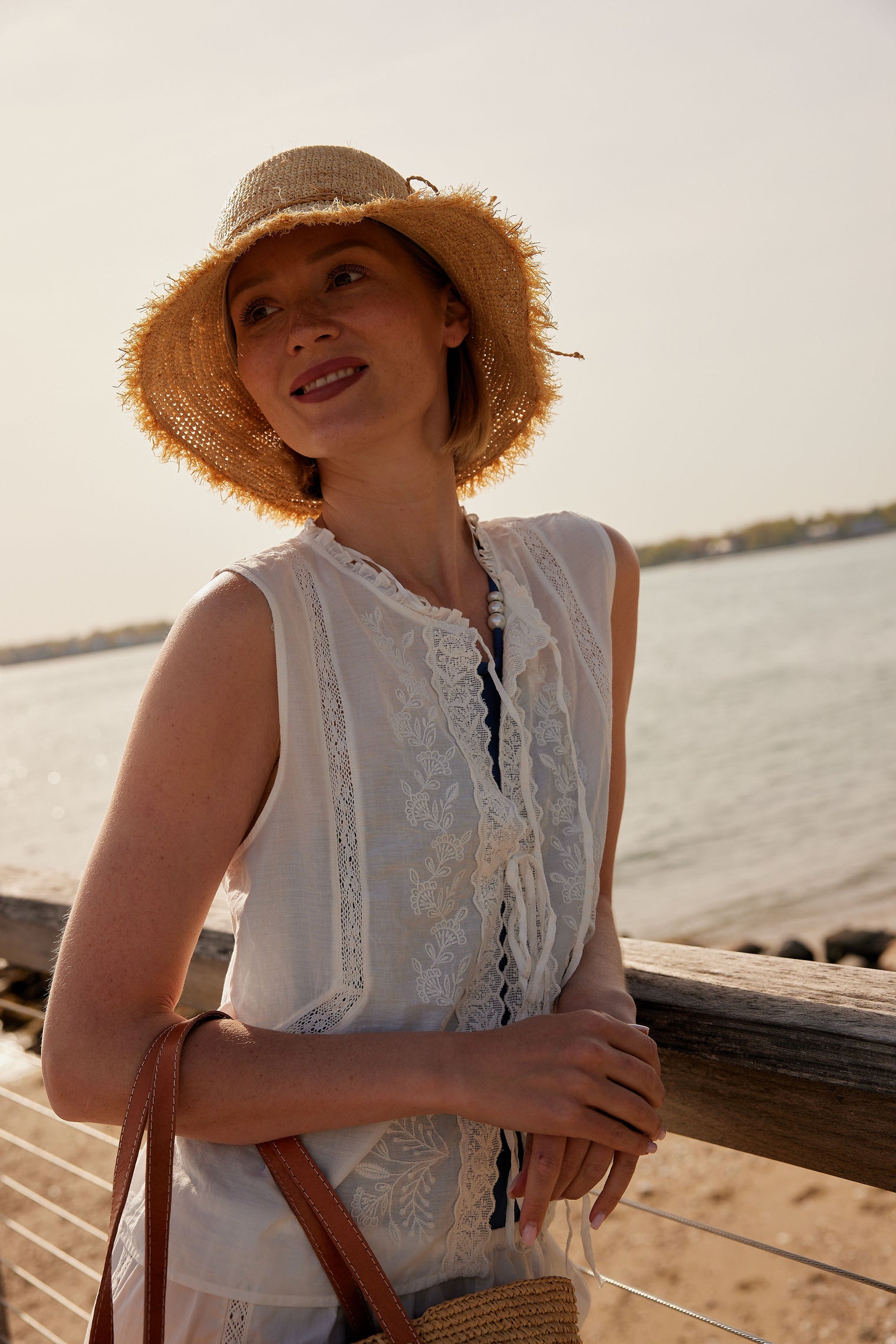 Model wearing a frayed edge straw raffia bucket hat on a pier