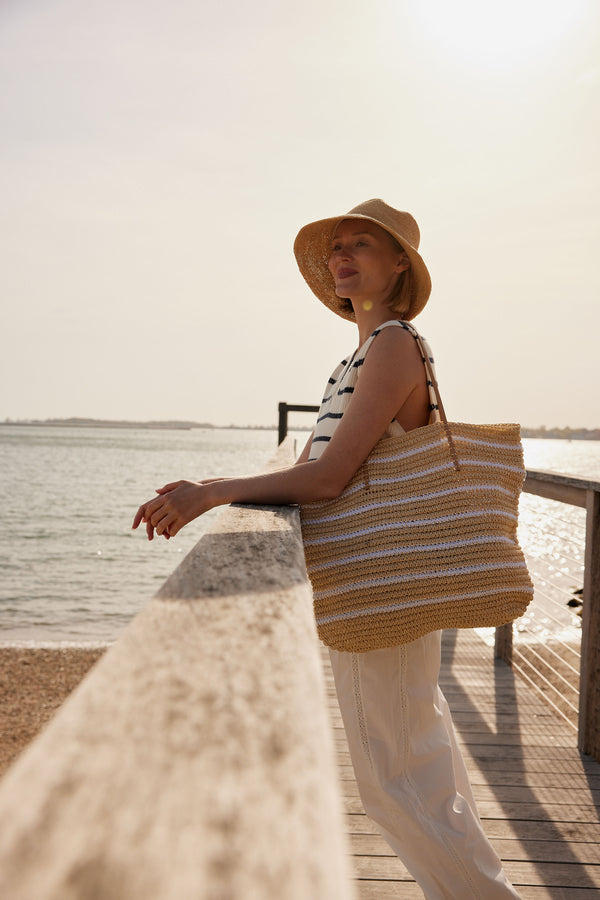 Model wearing white striped straw tote bag and straw bucket hat