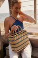 Model holding blue striped tote and wearing blue bathing suit