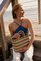 Model holding blue striped tote and sitting on pier