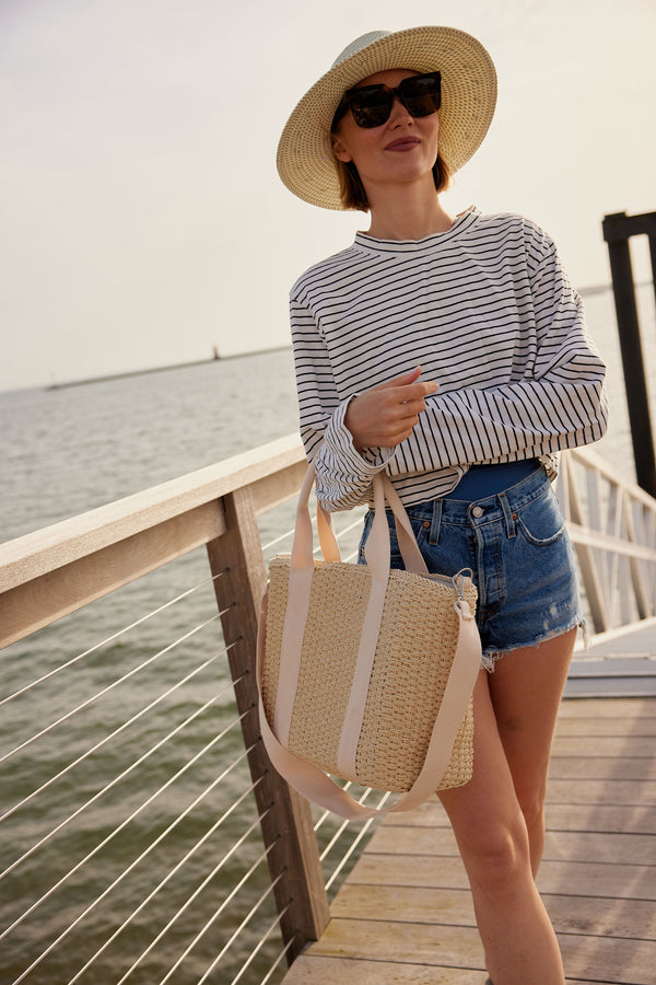 Model holding a straw cooler tote while standing on a pier
