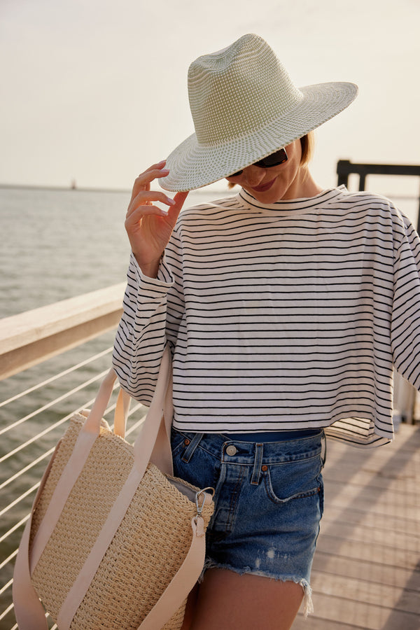 Model holding brim of green and white sunhat and straw cooler tote