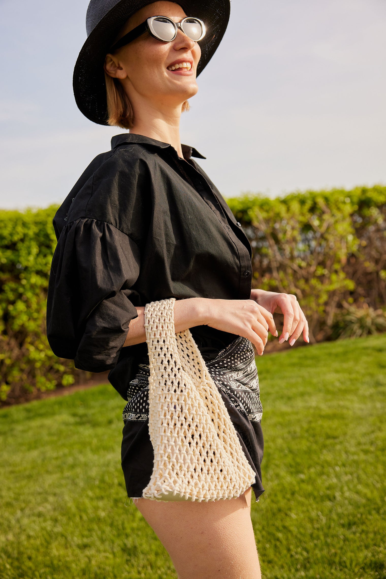 Model holding light tan cotton mini bag and black outfit