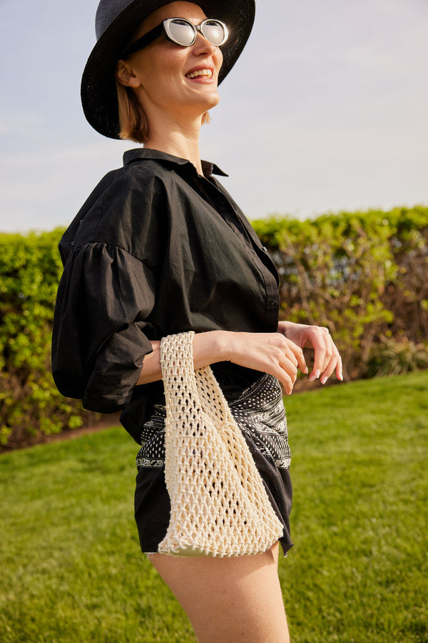 Model holding light tan cotton mini bag and black outfit