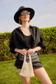 Model holding light tan cotton mini bag and black sunhat