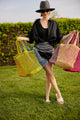 Model holding an assortment of colorful straw fisherman bags