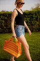 Model walking and holding coral and yellow striped tote bag