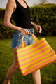 Close up of model walking and holding coral and yellow striped tote bag
