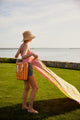 Model holding coral and yellow striped cooler bag and beach blanket