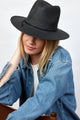 Model wearing black straw fedora and denim shirt while sitting in chair