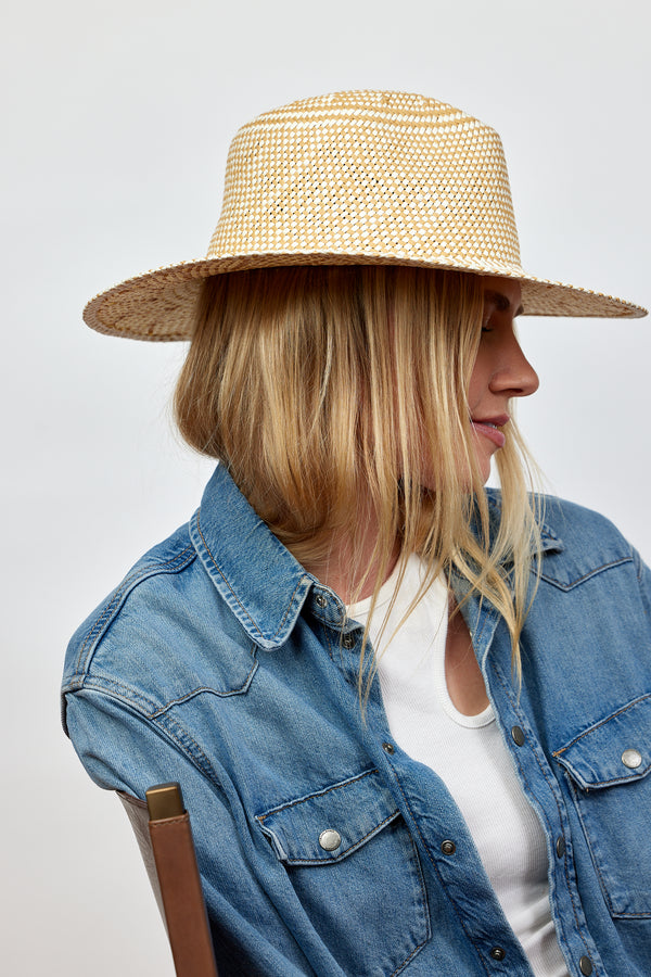 Model wearing tan and white woven sun hat while sitting in chair