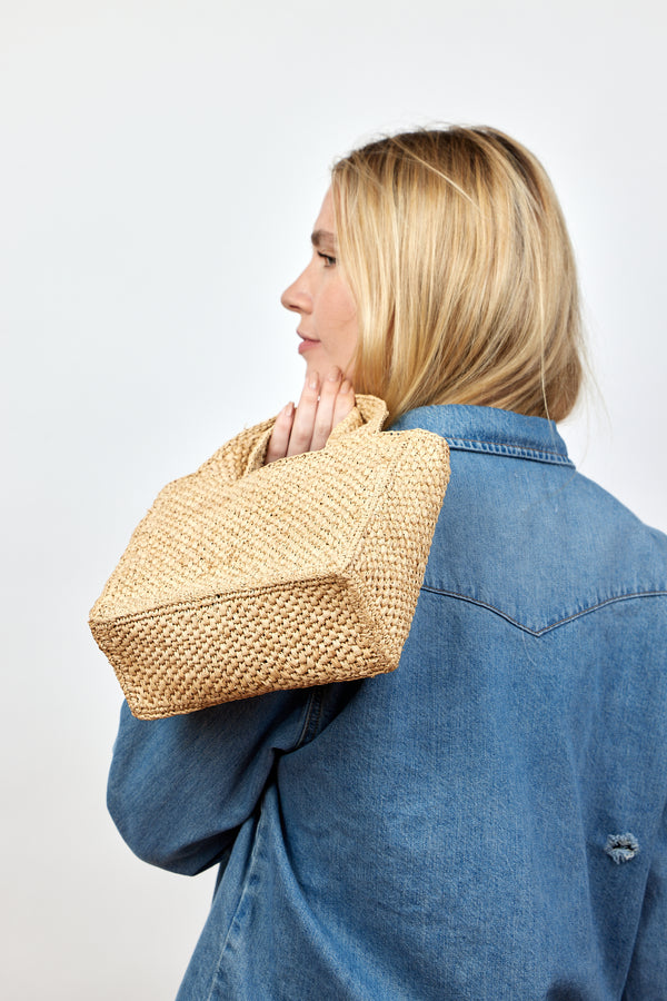 Model holding small structured woven straw bag and wearing a denim shirt