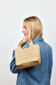 Model holding small structured woven straw bag over her shoulder