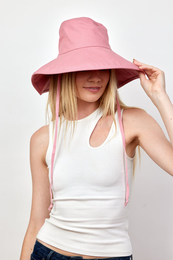 Model wearing and holding brim of pink canvas sun hat