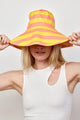 Model wearing coral and yellow striped bucket hat and holding brim