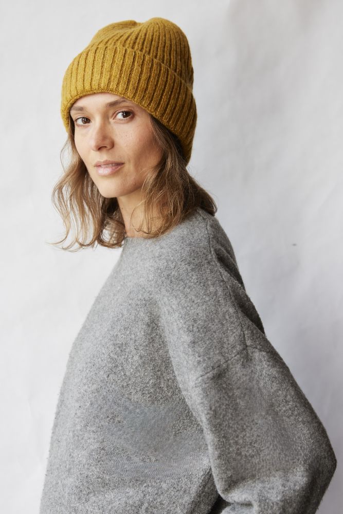 Woman wearing a mustard yellow beanie and gray sweater against a white background