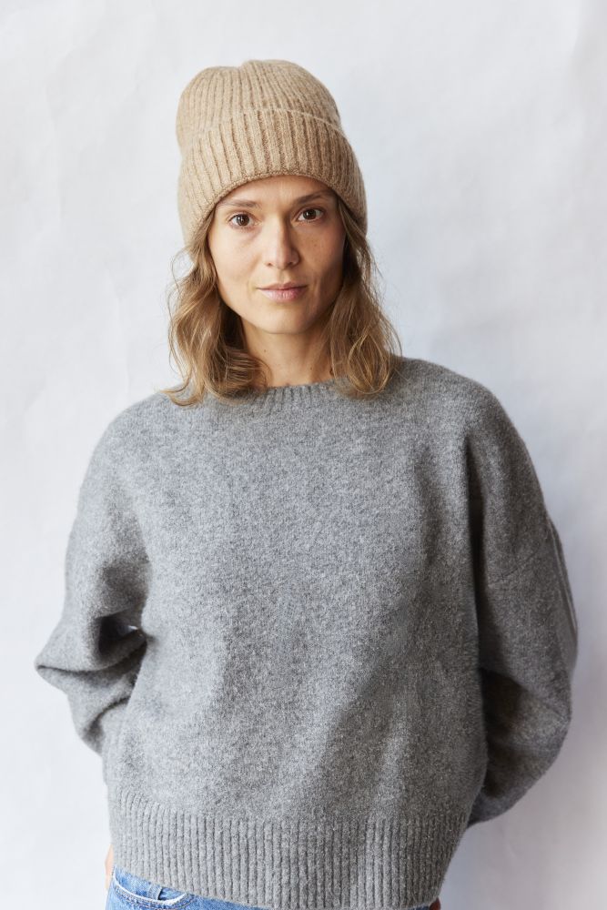 Woman wearing a gray sweater and beige beanie against a white background