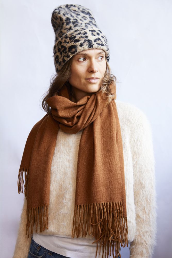 Woman wearing a leopard print beanie and brown scarf against a white background