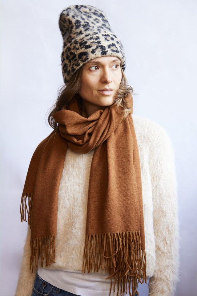 Woman wearing a leopard print beanie and brown scarf against a white background