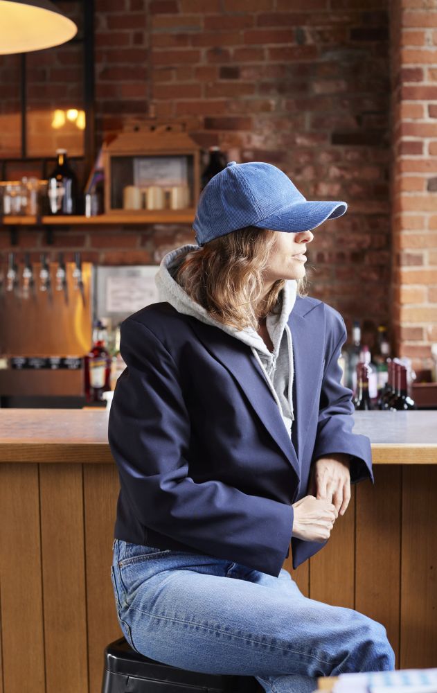 Woman wearing a blue cap and jacket sitting at a bar counter with a brick wall background