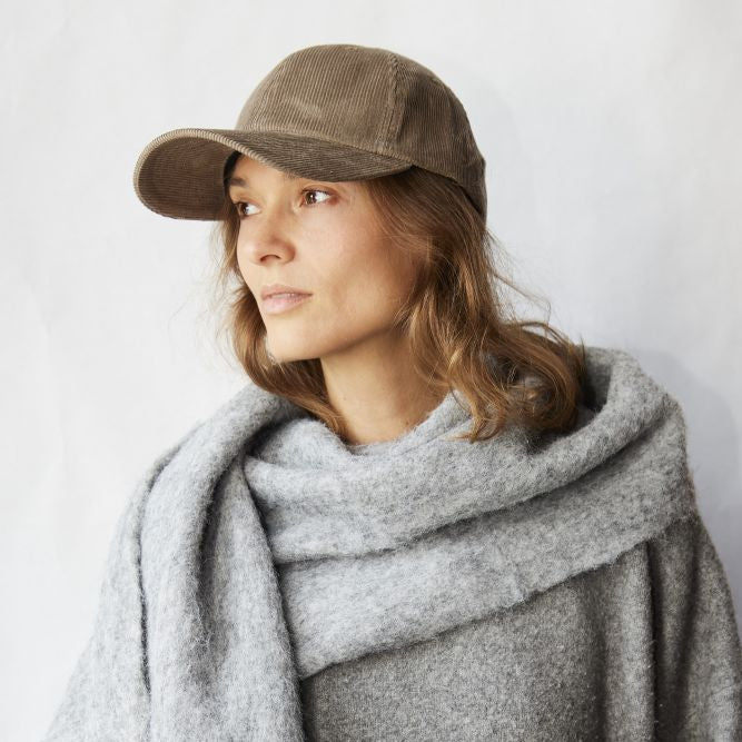 Woman wearing a brown cap and gray scarf against a white background