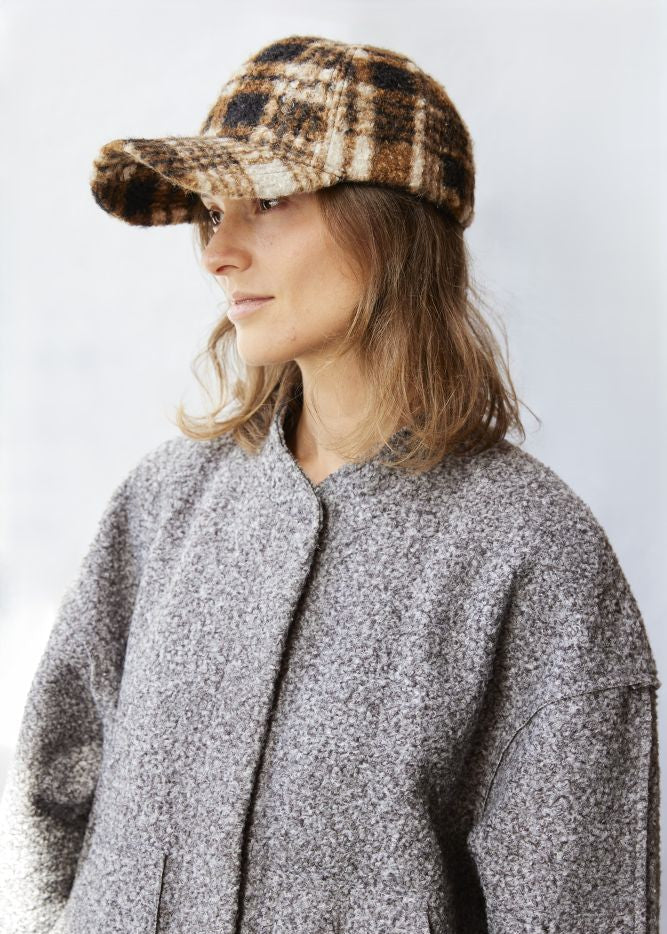 Person wearing a plaid cap and gray coat against a white background