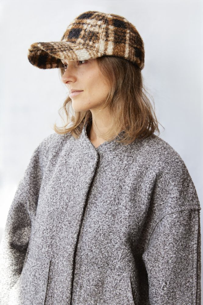Person wearing a plaid cap and gray coat against a white background
